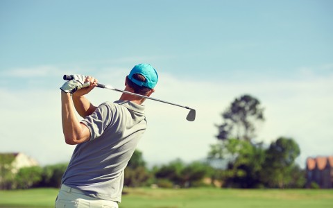 man swinging a golf club on a green golf course 